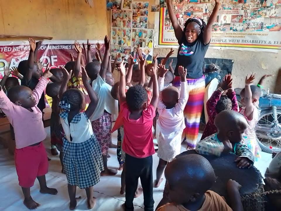 A play leader and pre-school children with their arms raised at the Joy of Play playgroup in Kampala